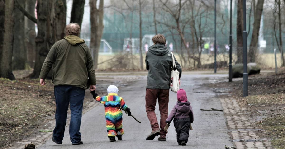 Four people walking away from the camera, two of them are small children