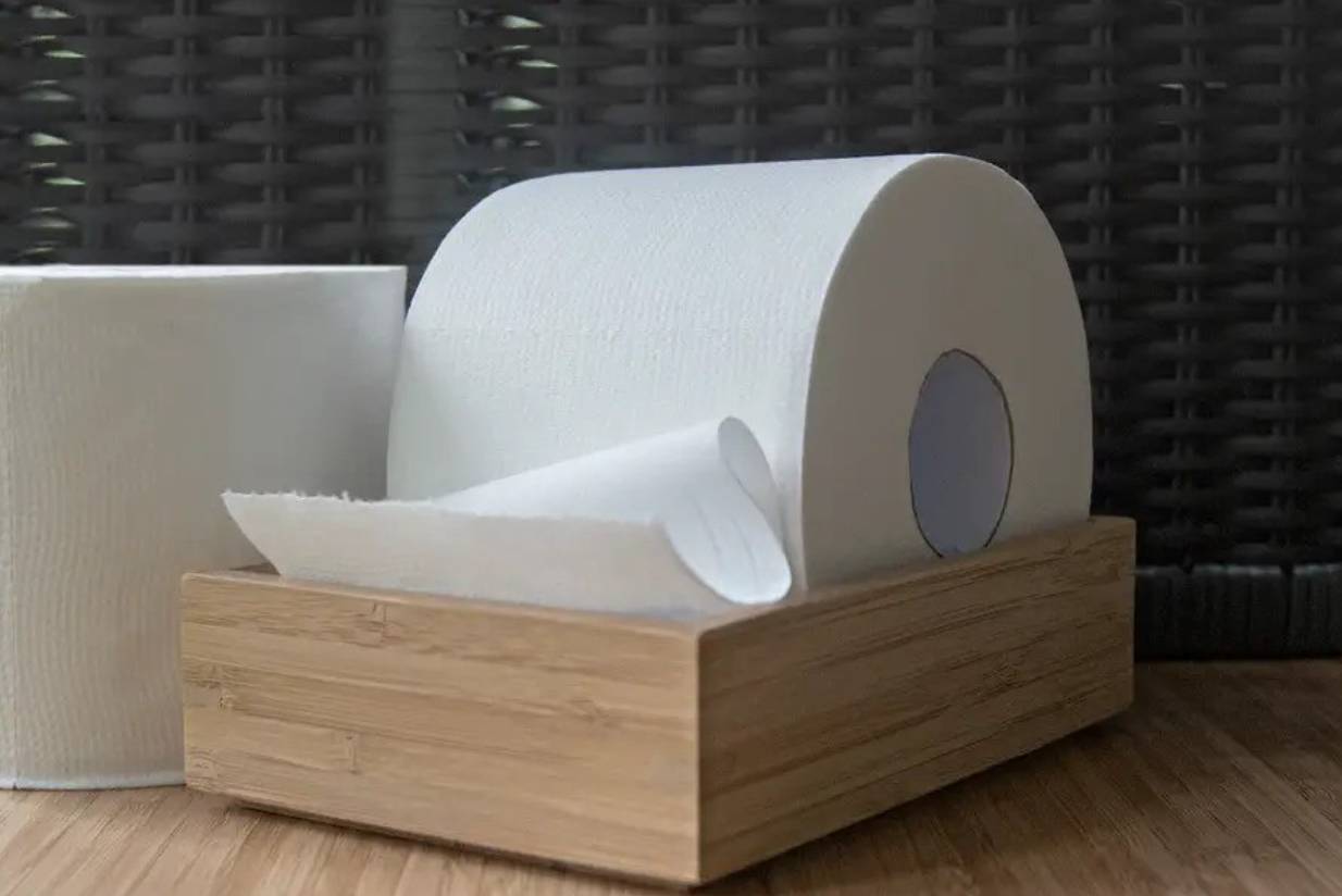A roll of white toilet paper sitting in a small wooden box next to another roll of toilet paper