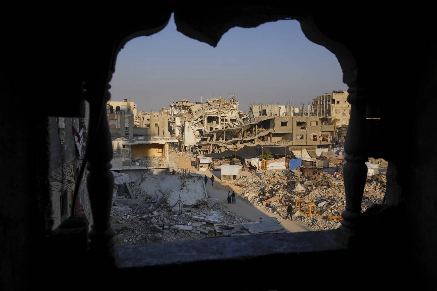 A handful of people walking through rubble in Gaza, pictured from a higher story in another building