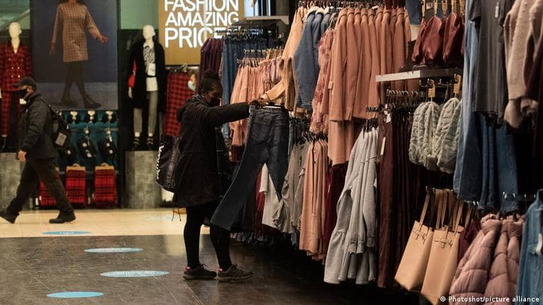 A person looking at a pair of jeans in front of a wall filled with clothing items