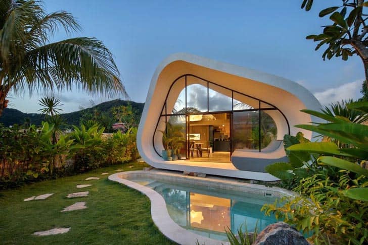 A tear-drop-shaped home with a small pool in front of it with a tropical environment around it
