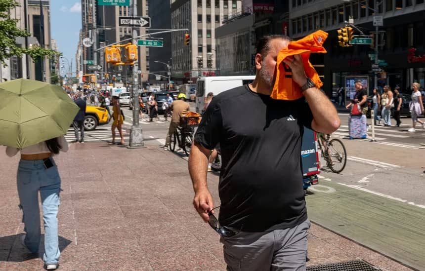 A man wipes sweat off his face with an orange towel on a sidewalk in Manhattan, New York City
