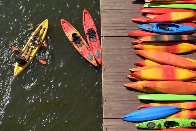 A pile of kayaks on a dock next to three kayaks in the water