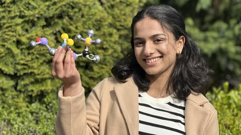 A person wearing a tan coat holding a molecule model structure
