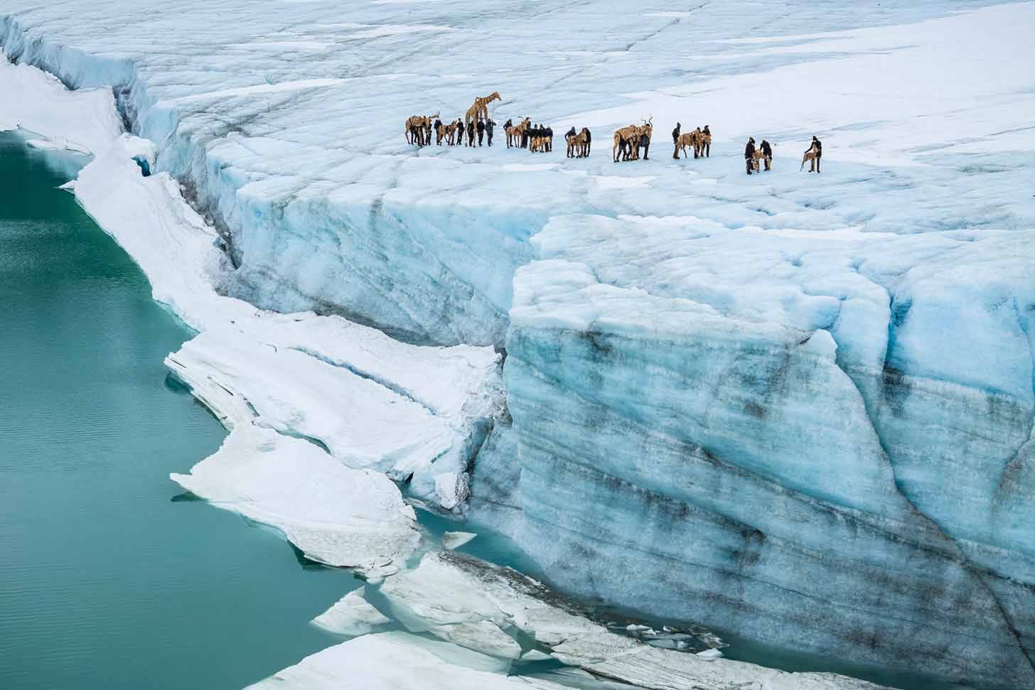 The side of a glacier with people and massive puppets walking along the edge