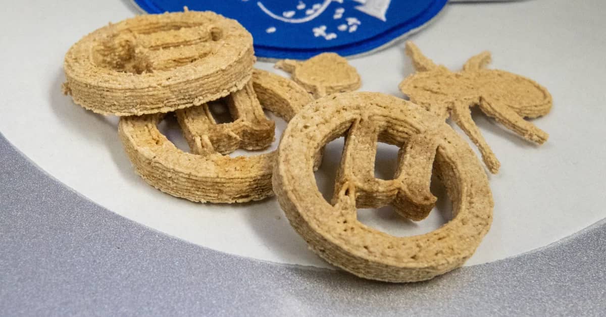 Tan-colored spiral pastries arranged on a white plate, including one coiled pastry and several curved, pretzel-shaped pieces. A blue plate is partially visible in the background.