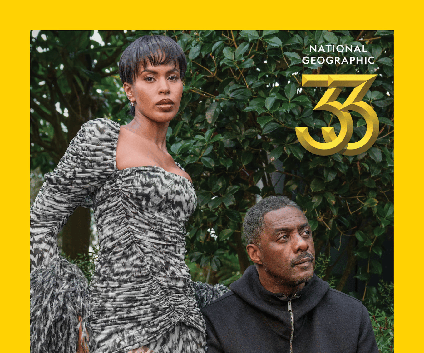 Idris and Sabrina Elba posed in front of a bush, there's a yellow border around the image and a graphic that says "National Geographic 33"