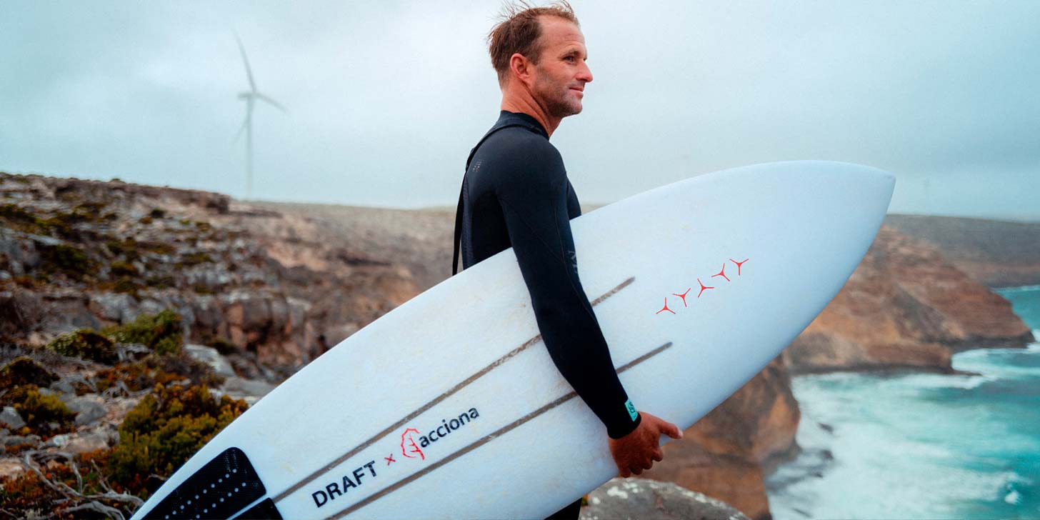 A surfer in a wetsuit holding a surfboard next to a body of water