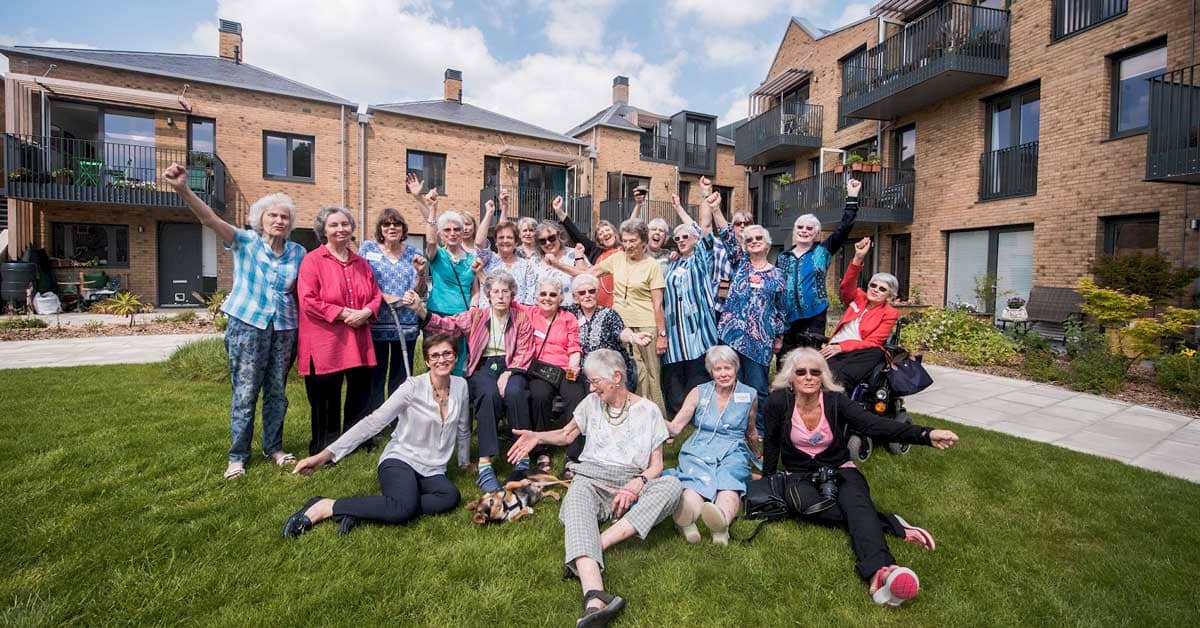 A group of women standing and sitting on a grass lawn with homes behind them, they're smiling, cheering