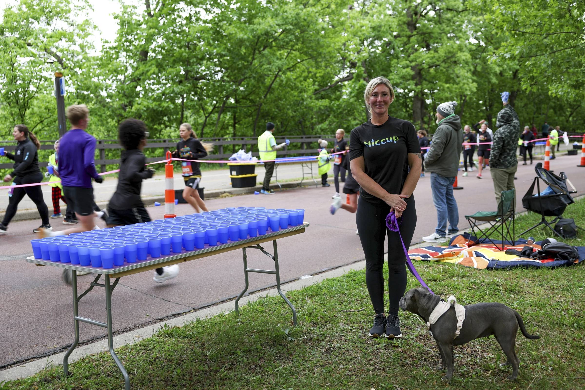 Kristina Smithe holding a dog on a leash next to a table filled with blue silicone cups