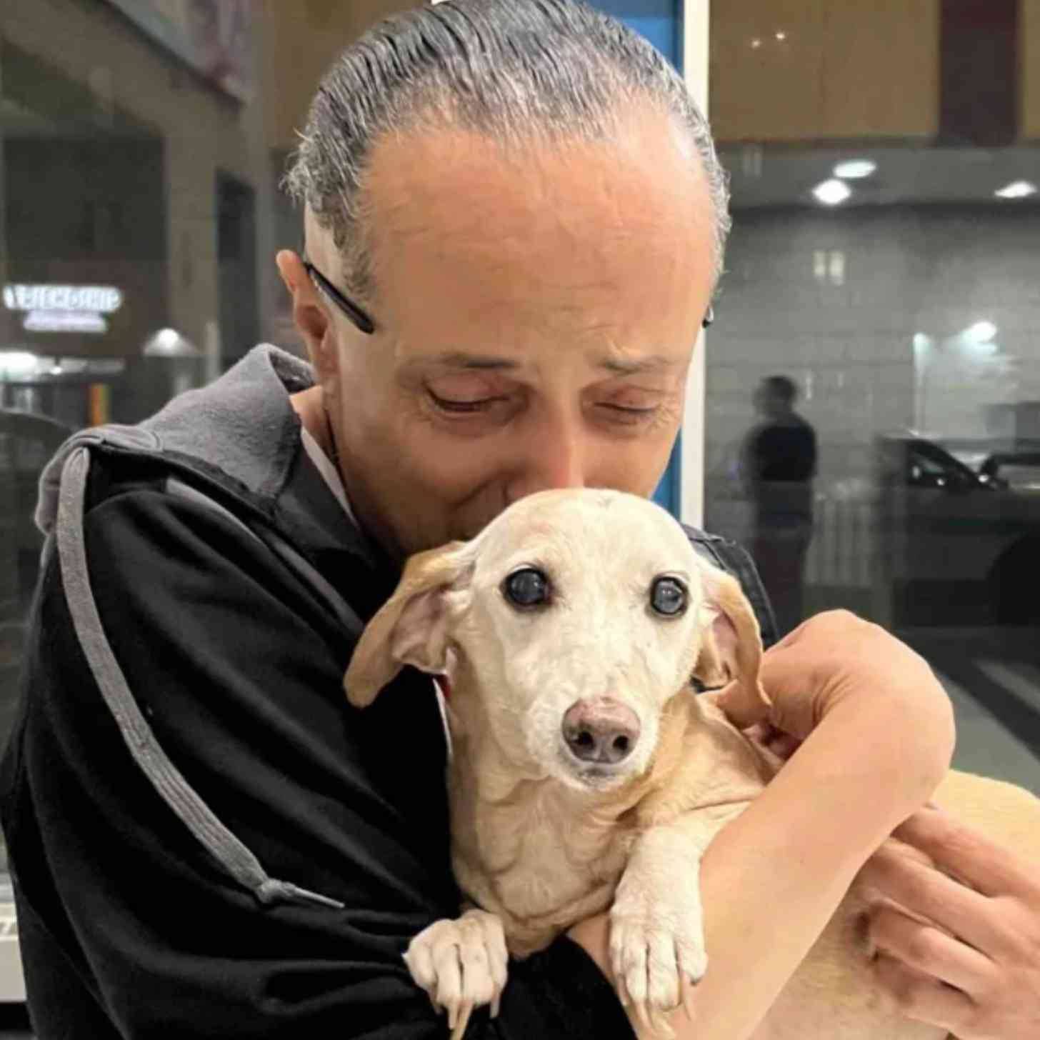 A man holding a light tan-colored dog, kissing it on its head