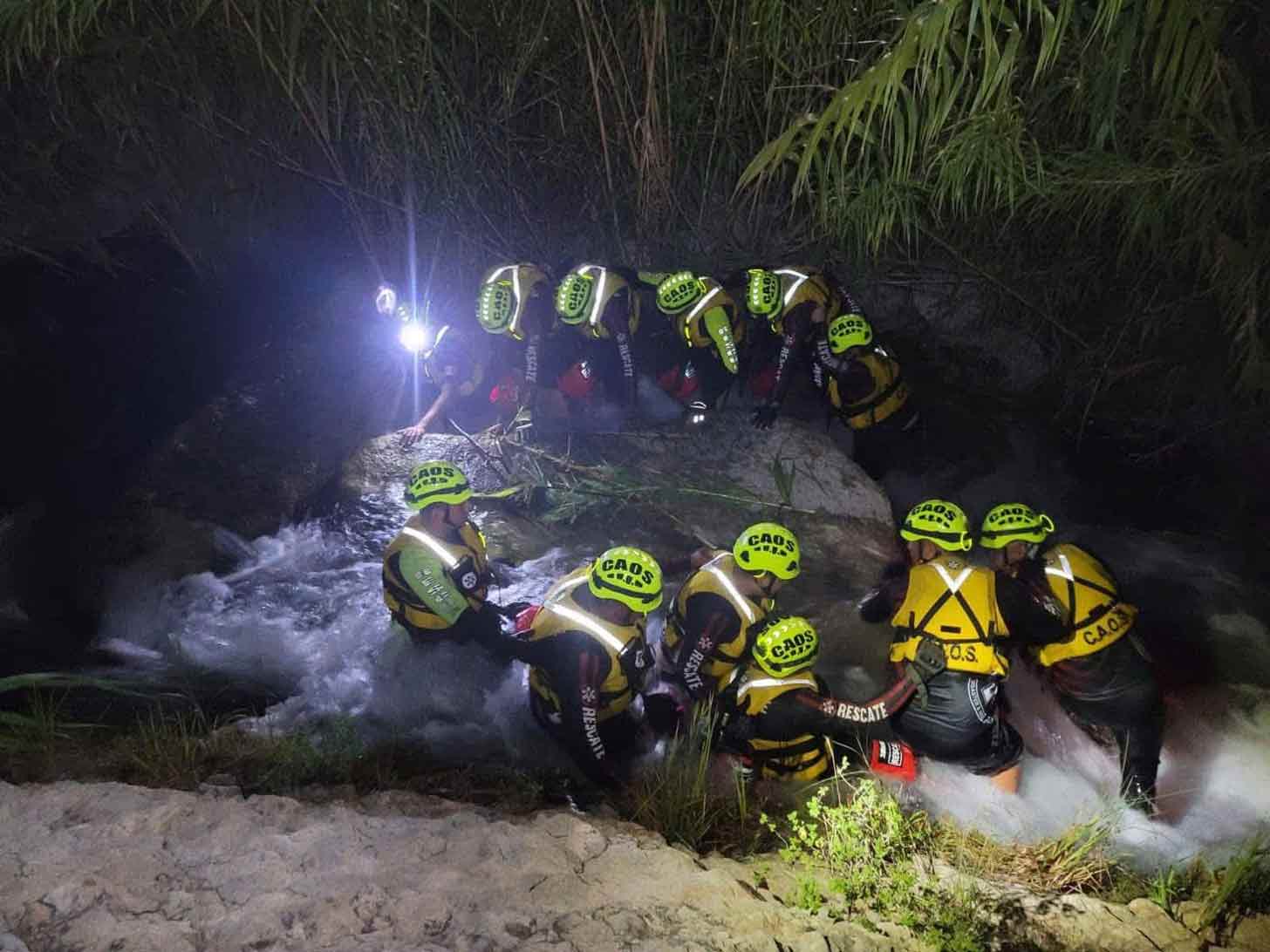 Twelve people in neon hats and yellow vests in a waterway at night