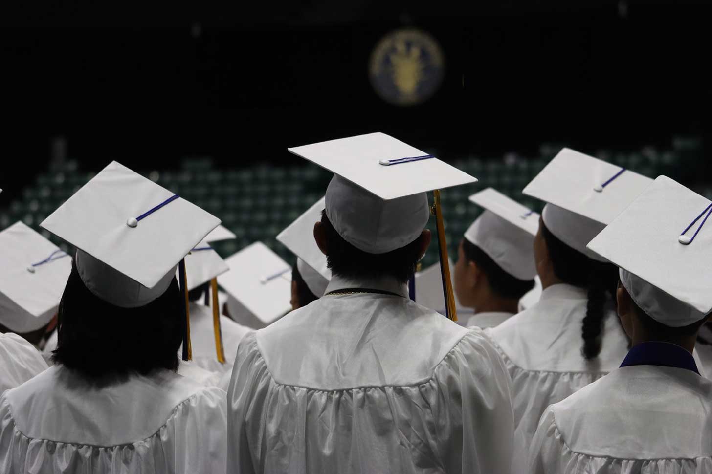 Graduates in white caps and gowns pictured from behind
