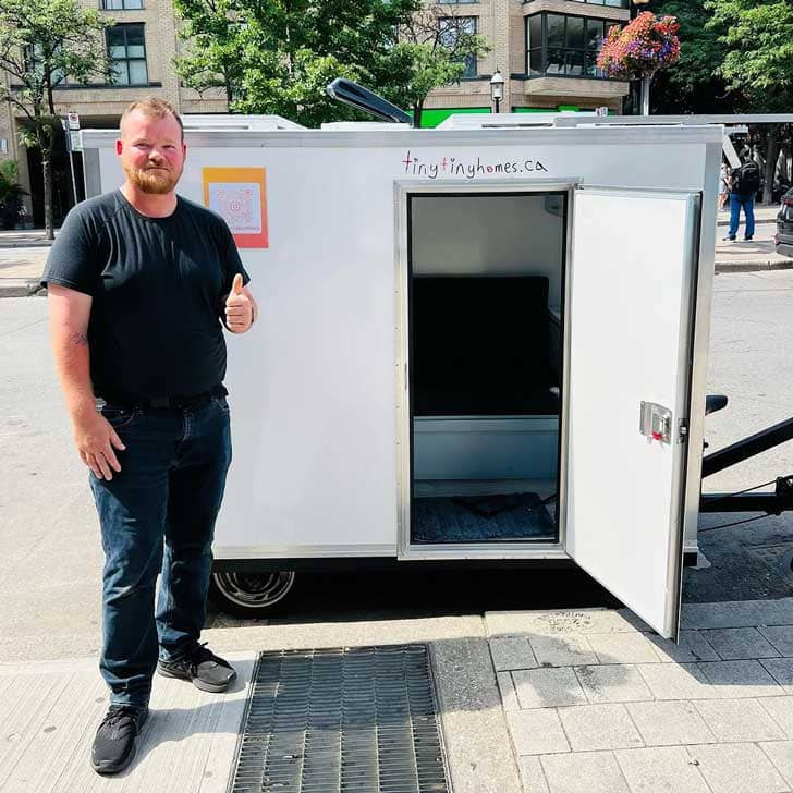 A person standing outside a tiny tiny home on the back of a bike