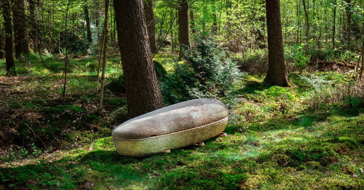 A white, dirt-covered, rounded casket in a forest nature scene