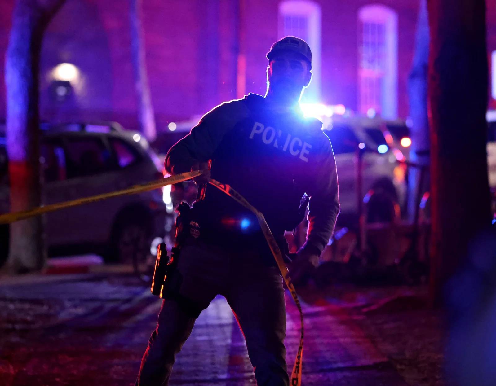 A police officer at night setting up crime scene tape in an alley