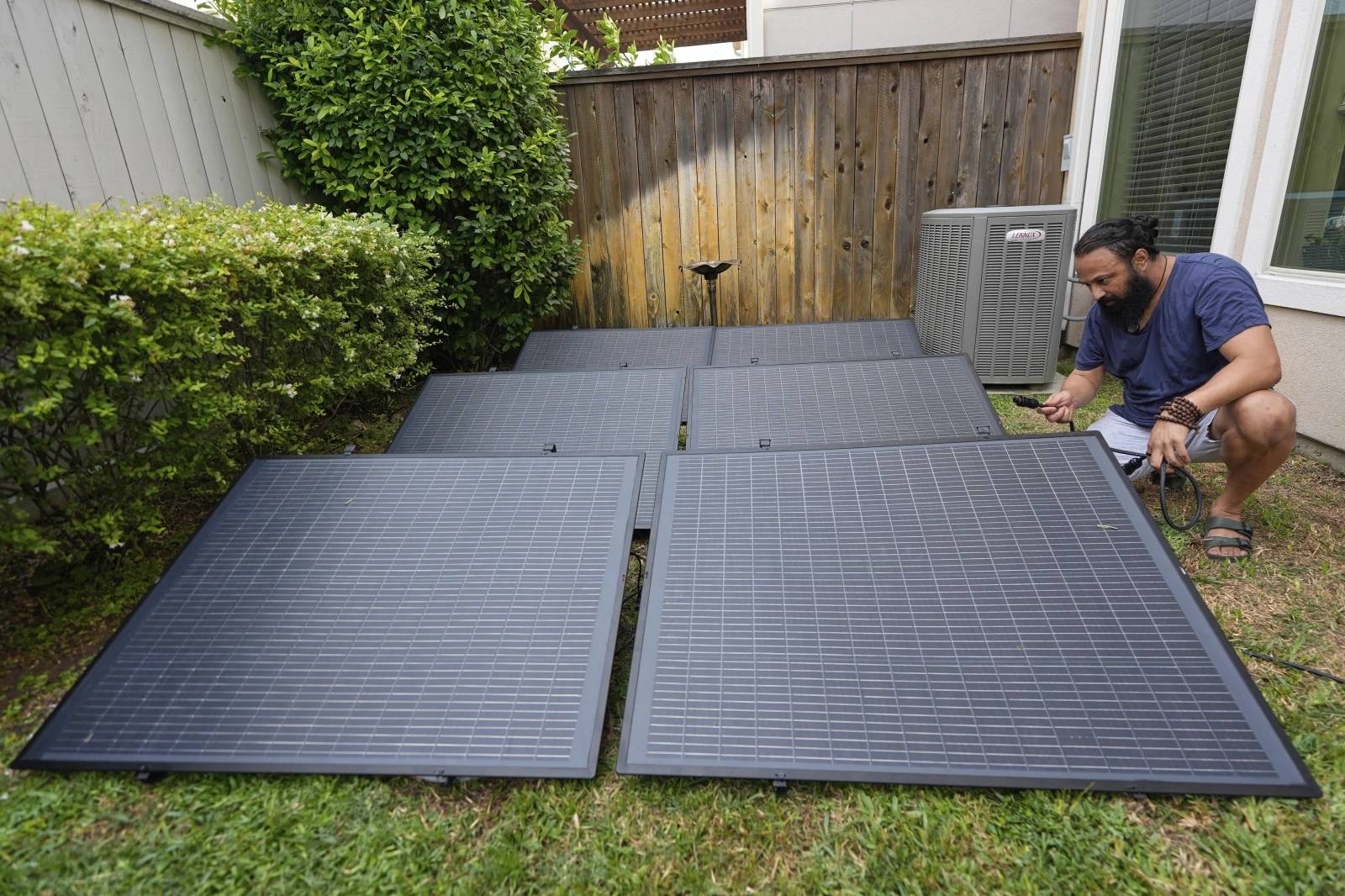 Six smaller square solar panels on a grassy ground, a person is crouching next to them