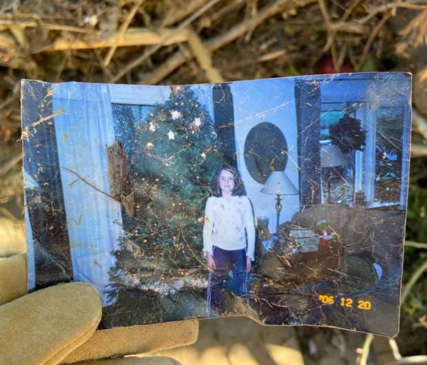 A tattered film photo of a young girl standing in front of a Christmas tree