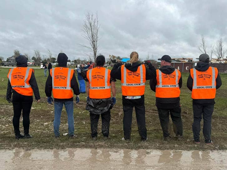 Members of Zach Bryan's tour team wearing orange work vests that say "The Quittin Time Tour"