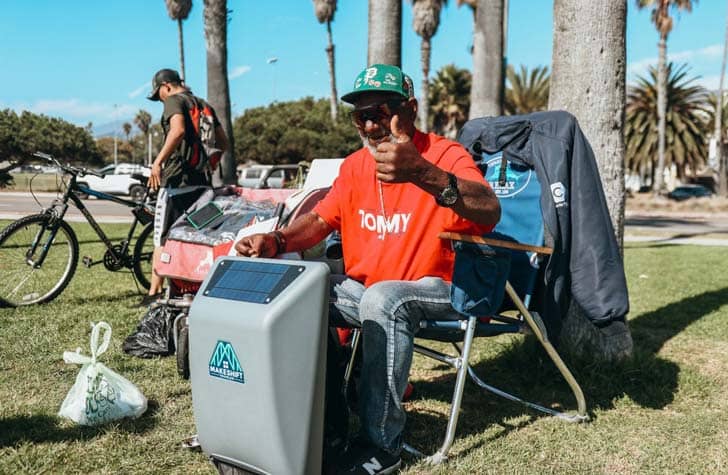 An unhoused person sitting in a chair with the makeshift backpack on the ground in front of them