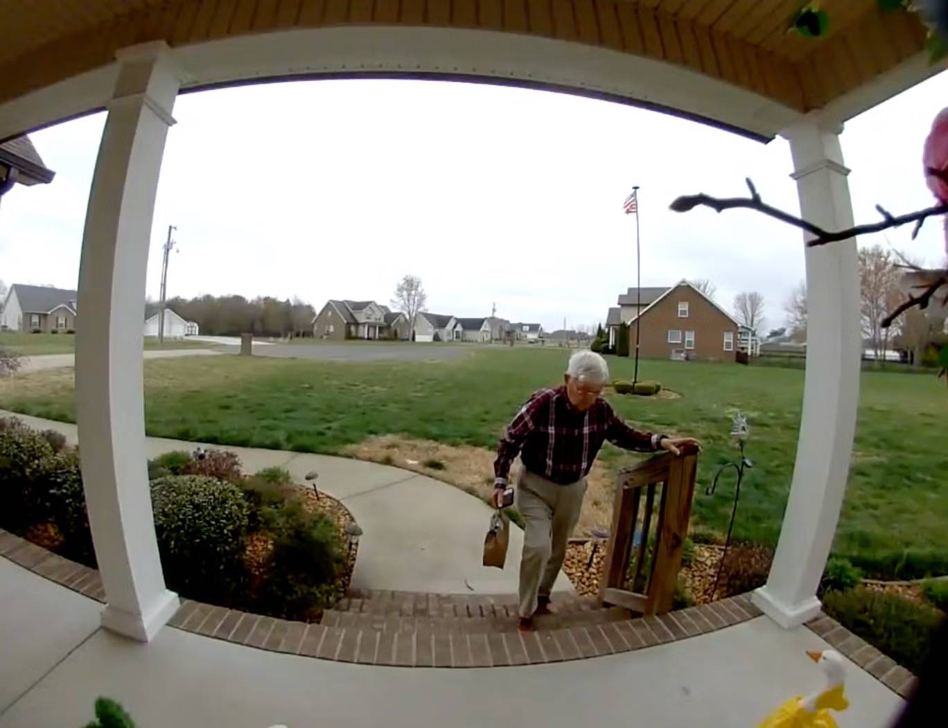 A man wearing khakis and a plaid button-down shirt holding a railing as he climbs up brick stairs holding a brown bag