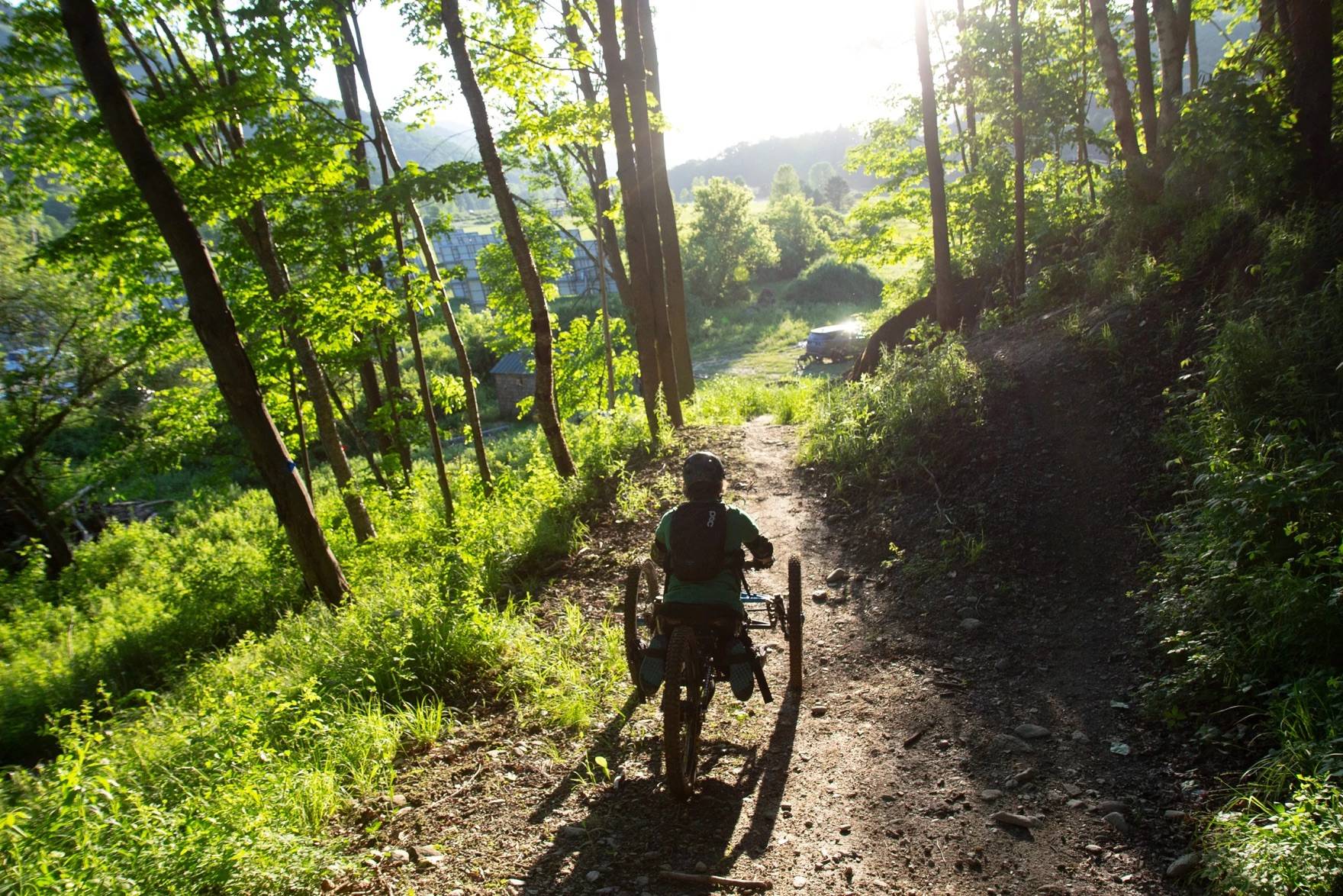 A biker on an adaptive mountain bike on a trail surrounded by trees