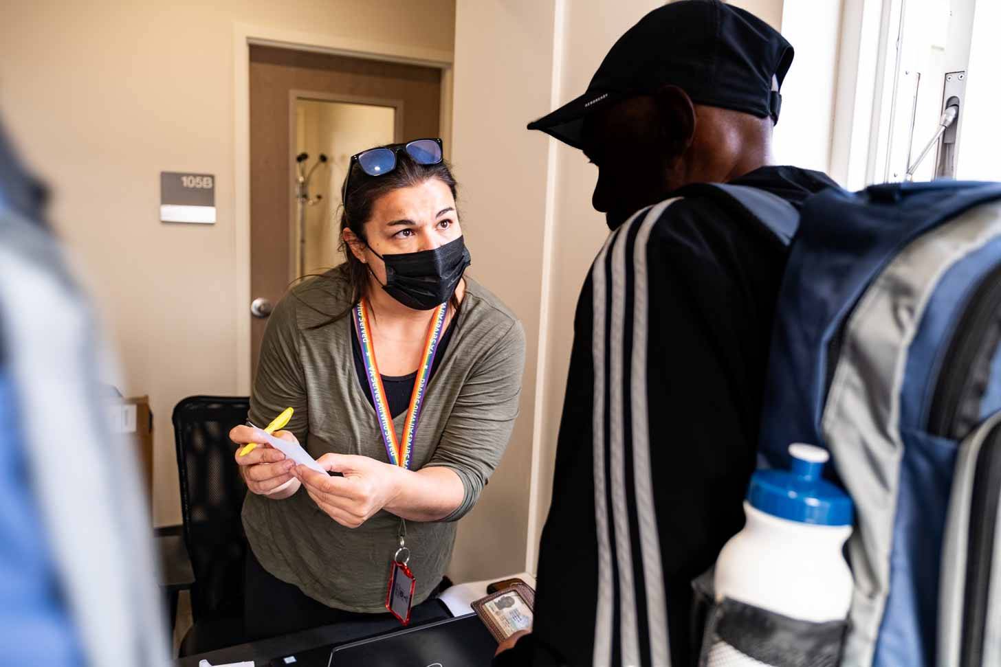 A person wearing a mask showing another person something on a piece of paper