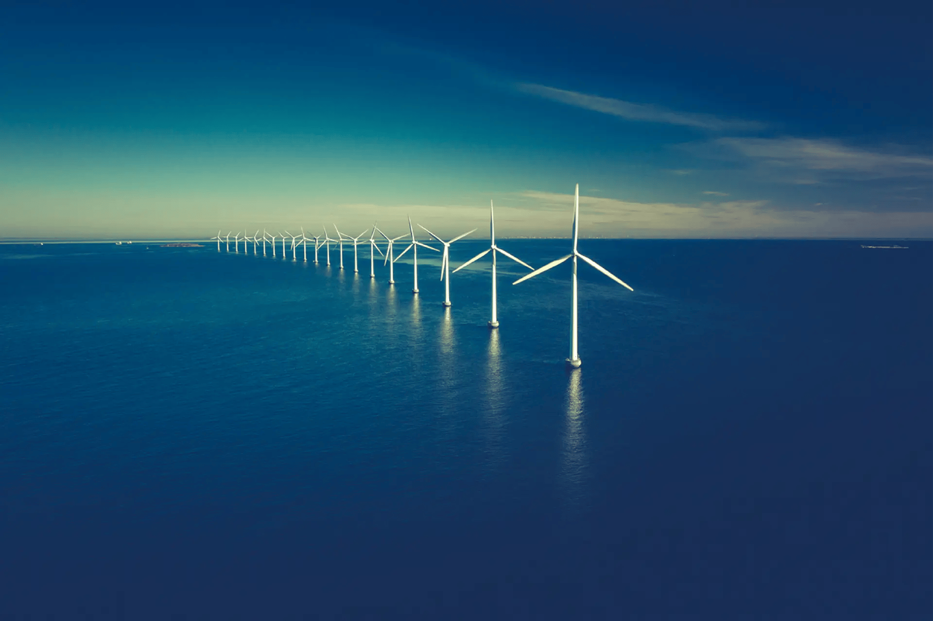 A line of white wind turbines in the middle of a blue water expanse
