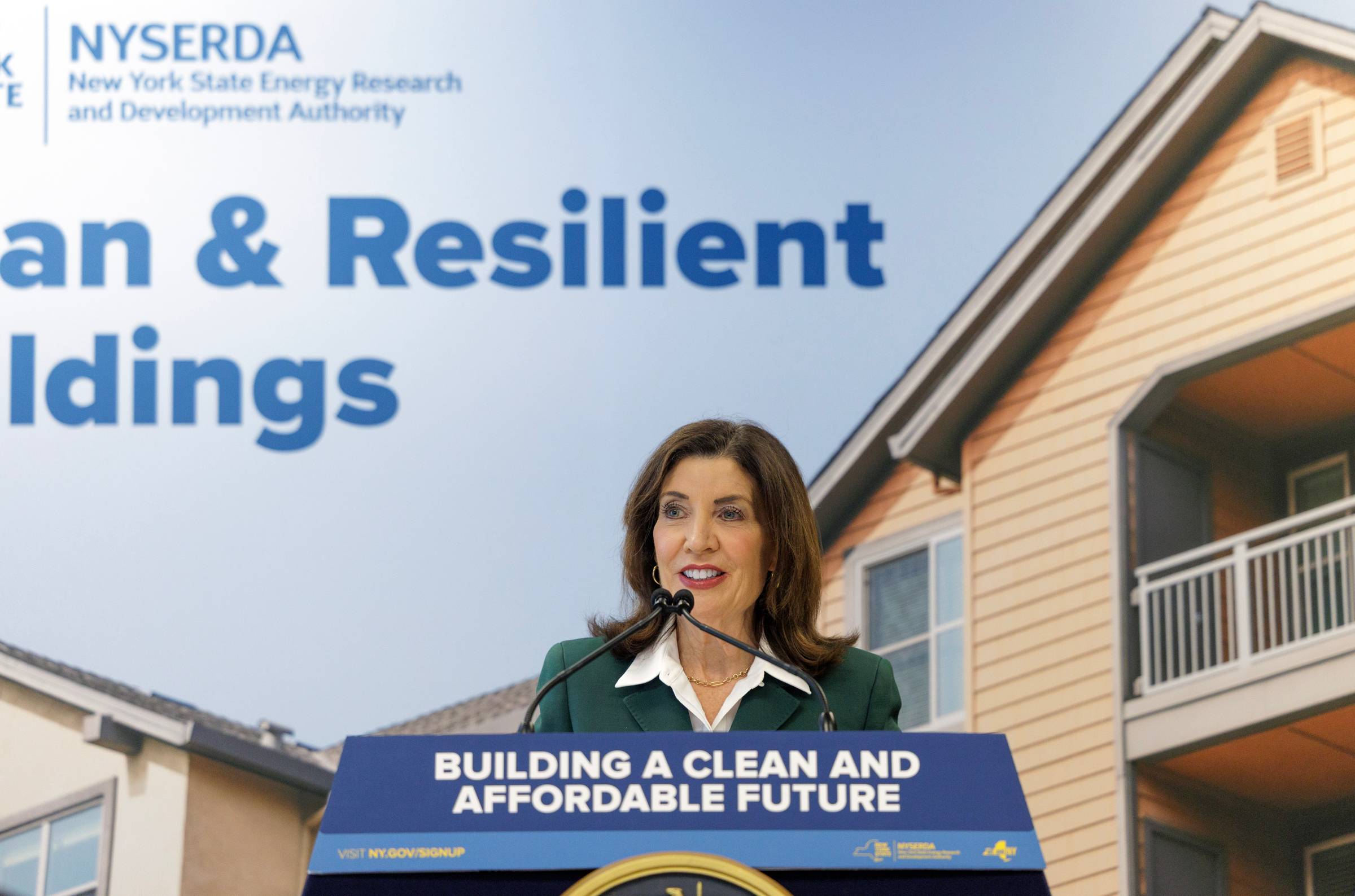 Governor Kathy Hochul talking into a microphone at a podium that says "Building a clean and affordable future"