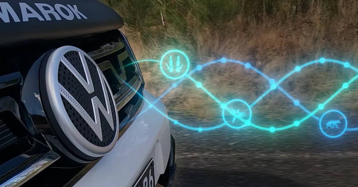 Close-up of the front end of a VW car, blue and green glowing waves are depicted in front of it, illustrating sound waves