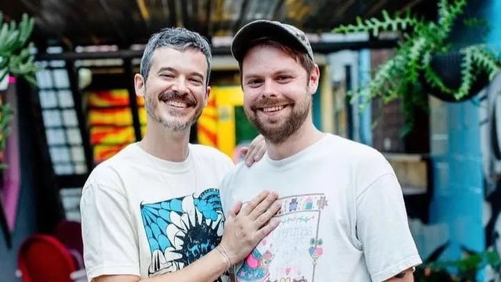 Branden Davis and Davie standing together smiling in front of a colorful building with plants hanging from the ceiling