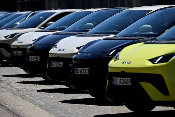 Row of electric vehicles parked in a line, including black, white, and bright yellow cars with visible license plates and "e10" badging on their sides.