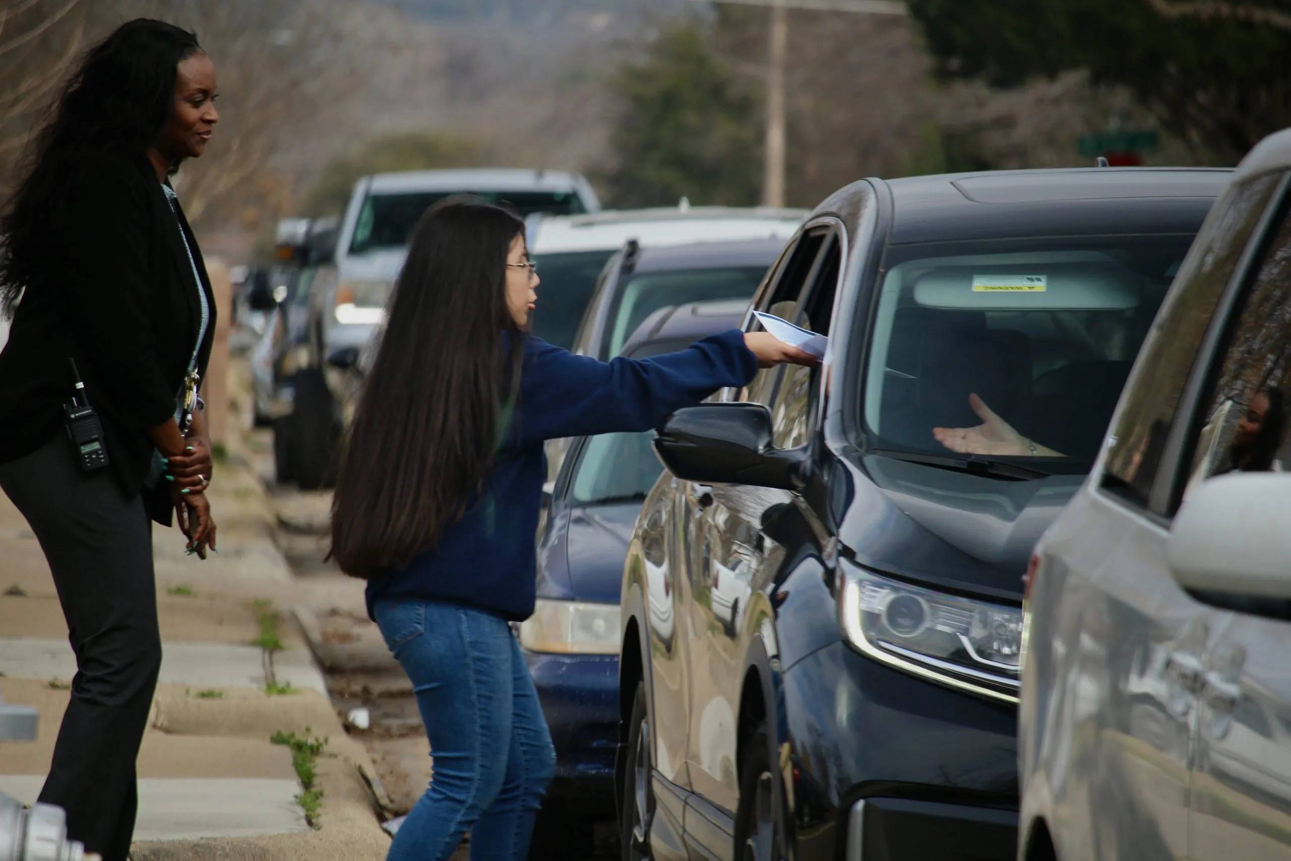 A student handing papers through a car window