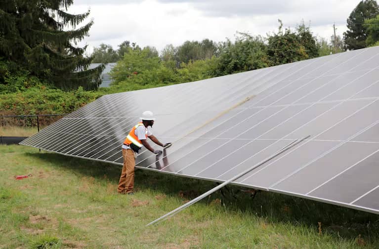 A person measuring a large solar panel installation in a grassy field