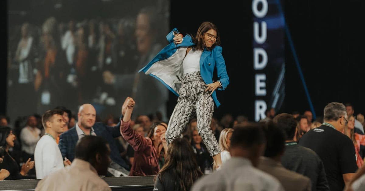 Woman in print pants and a real blazer dancing on a stage with people on the floor