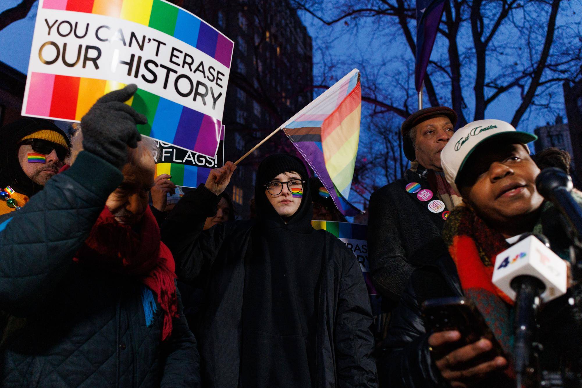 Crowd of people holding signs, waving pride flags
