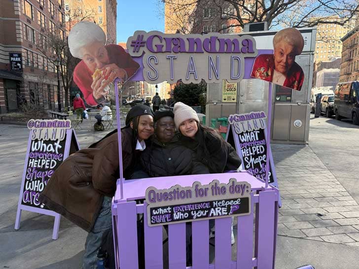 Three people behind a purple "lemonade" style stand
