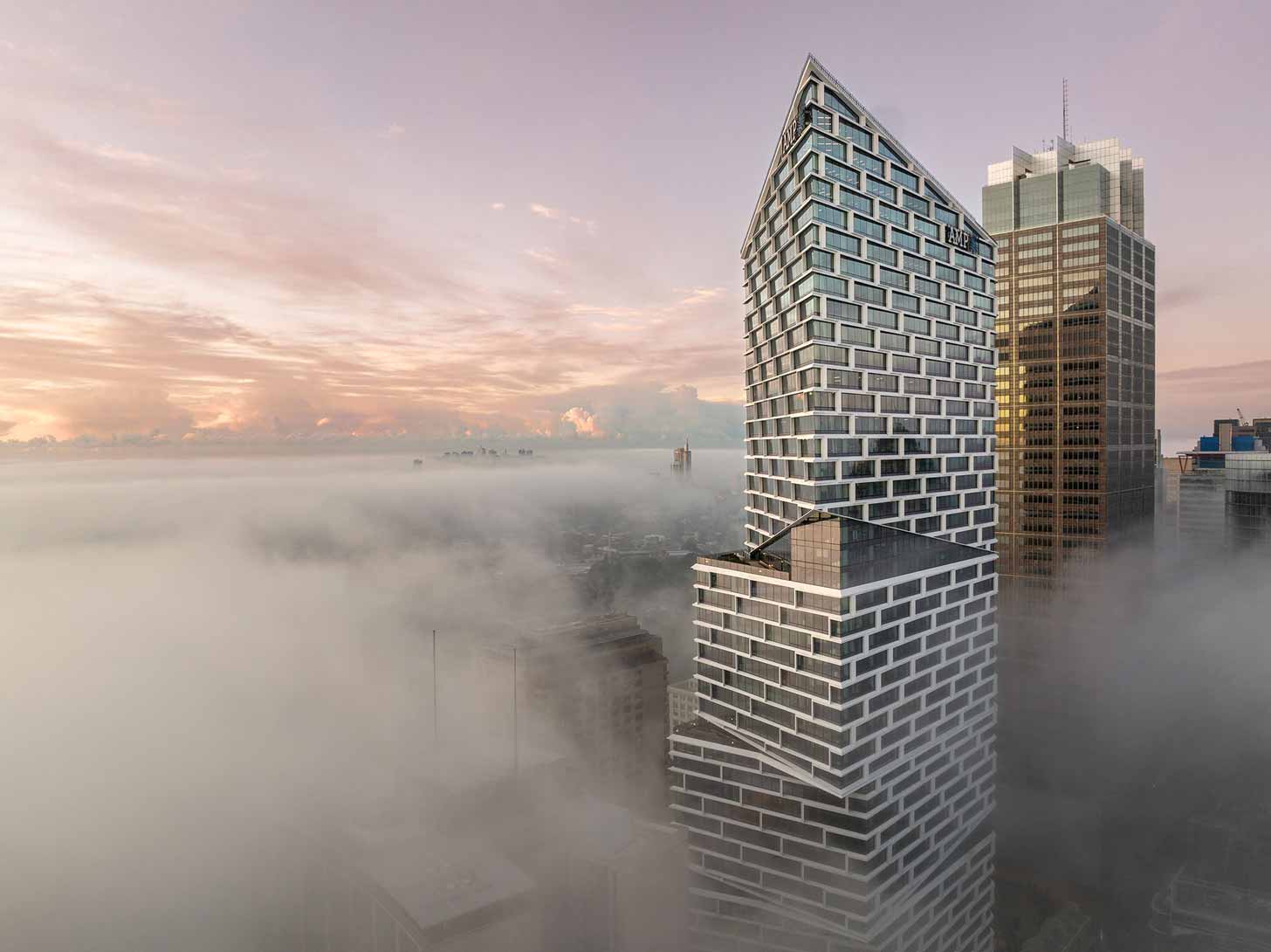 Top of a pointed skyscraper situated above the clouds at sunrise
