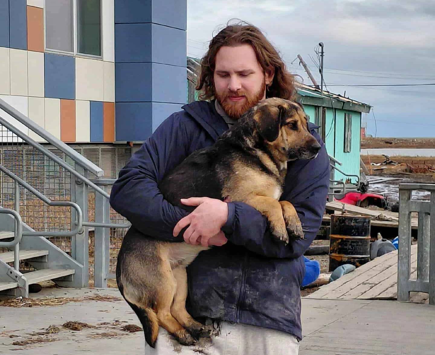 A person in a navy blue coat carrying a black and tan dog