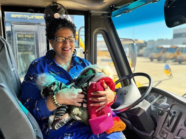 School bus driver in her driver's seat with an armful of hats