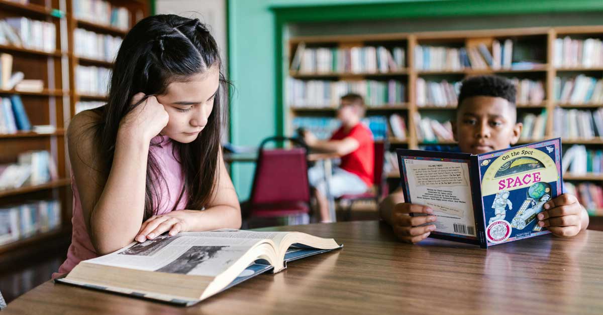 Two students reading in a library sitting at a table