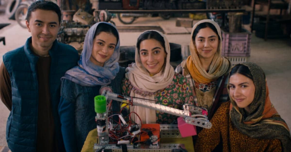 Five people, four of them women standing behind a robotic object