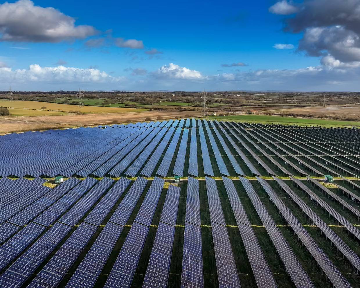 A field full of solar panels, a blue sky overhead and parcels of farm land in the distance