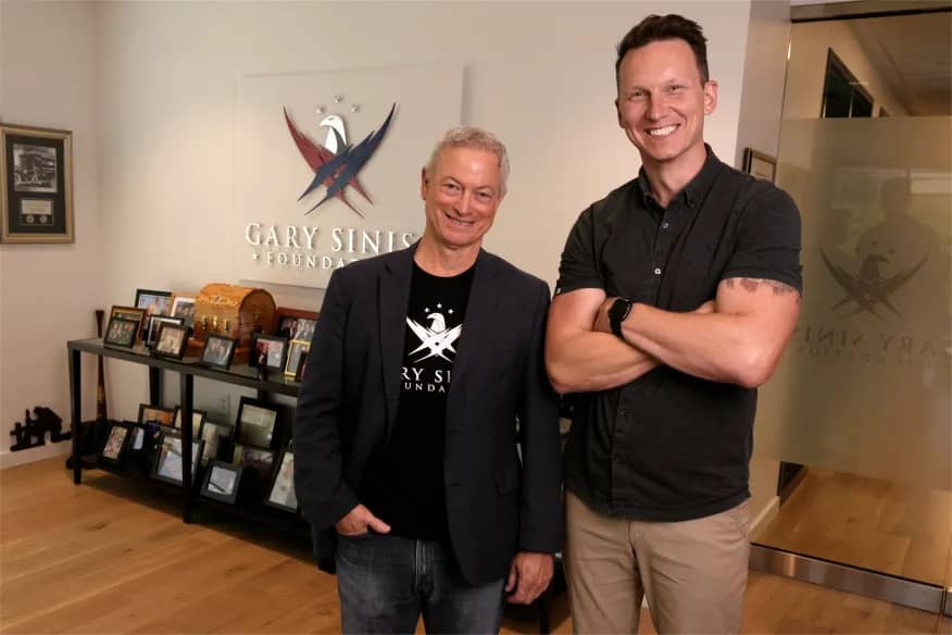 Gary Sinise and Richard Casper in a room with "Gary Sinise Foundation" on the wall behind them