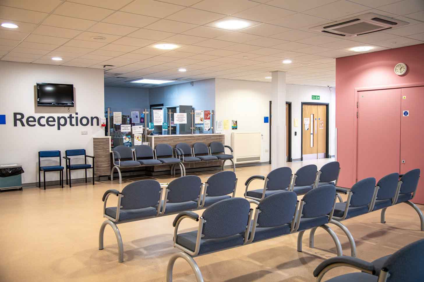A medical waiting room with "Reception" on the wall and groups of empty chairs