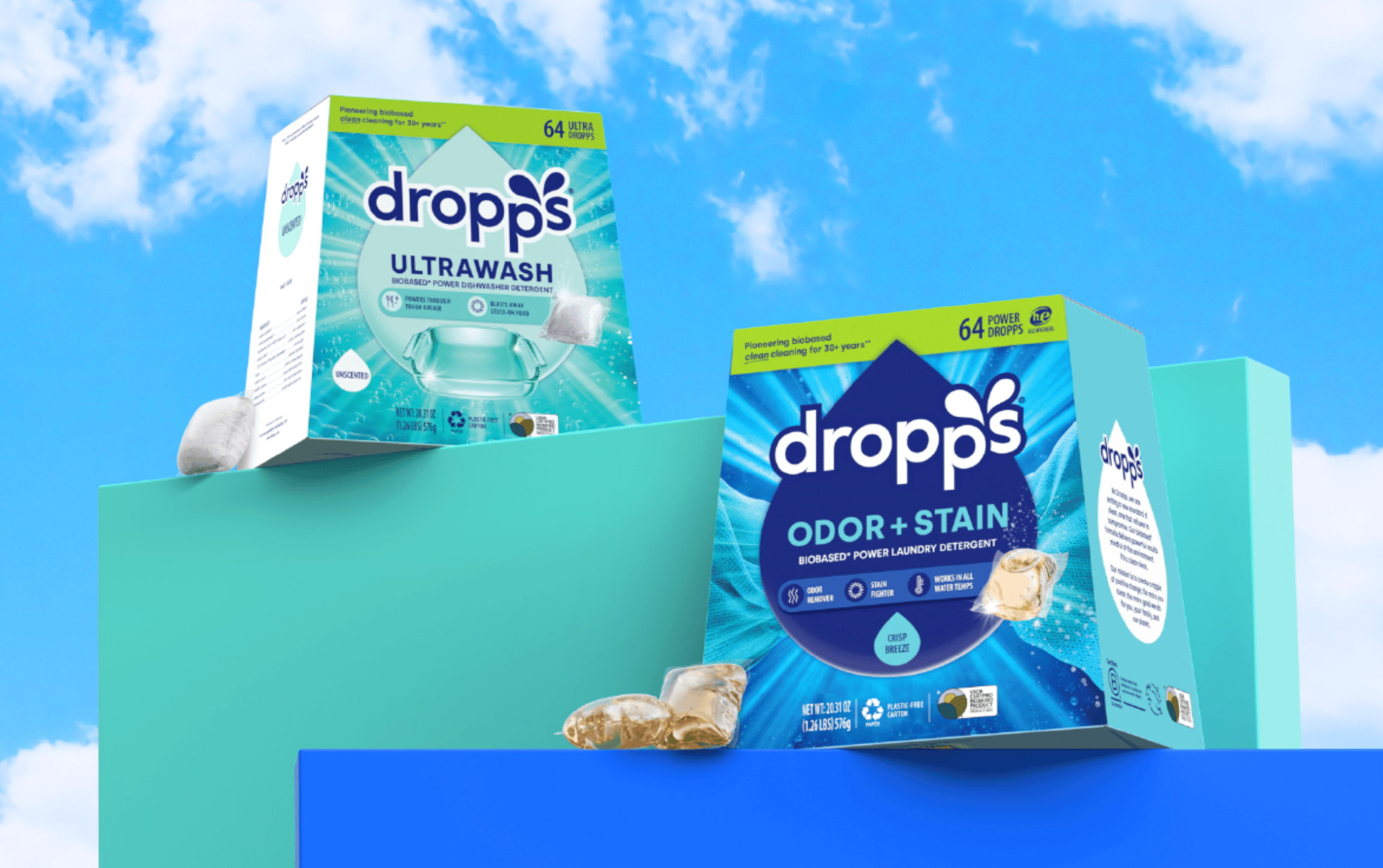 Two boxes of Dropps-branded boxes of dishwasher detergent and laundry detergent on colored boxes against a blue sky background