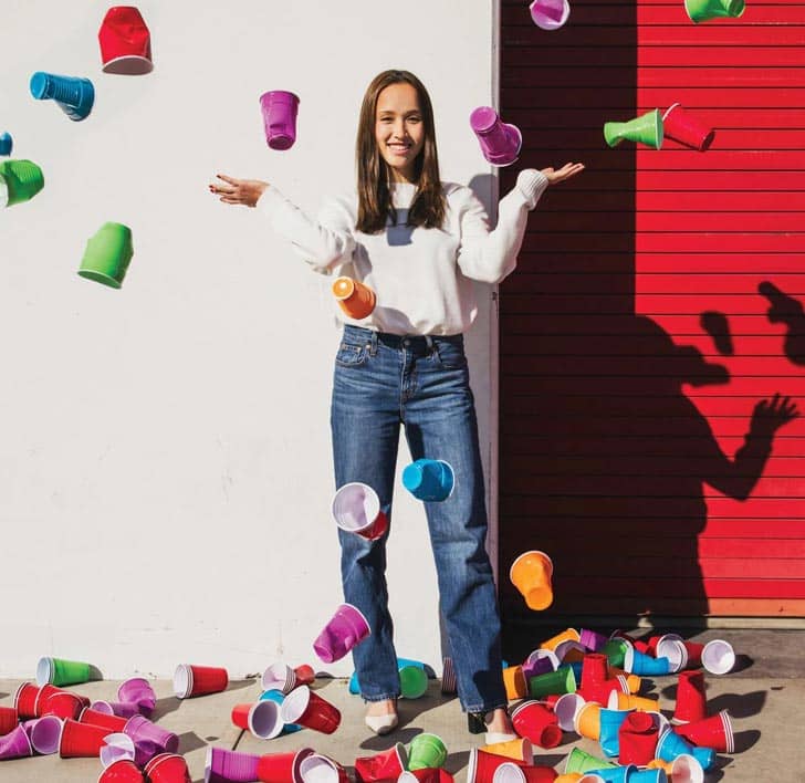 A person with long brown hair throwing colored plastic party cups in the air