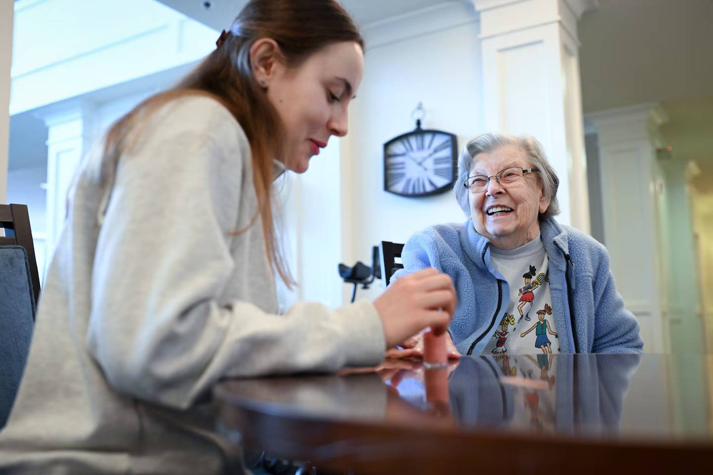 A younger woman painting an older woman's nails, they are both smiling