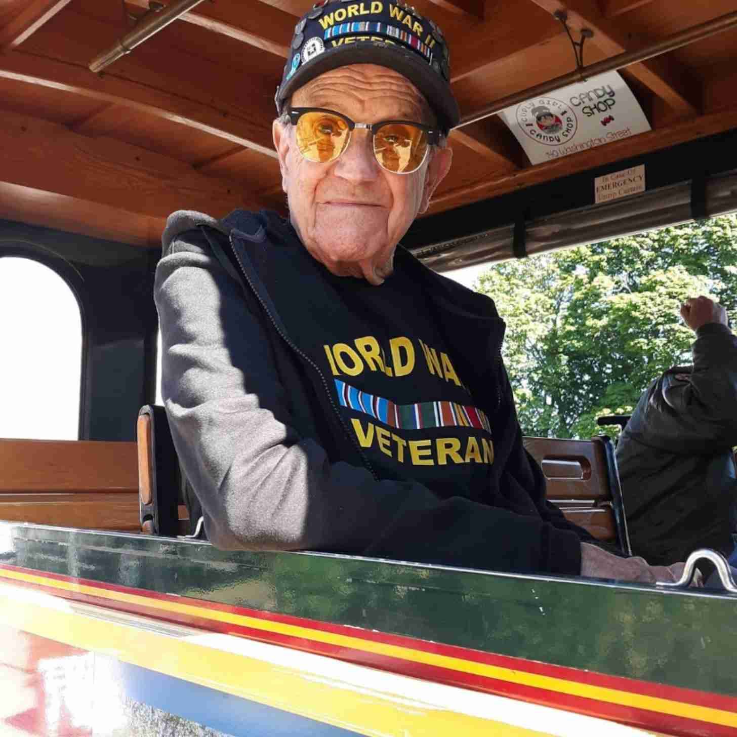 Leo Valente sitting in a trolley car looking out the window, he's wearing a "World War II Veteran" hat and shirt