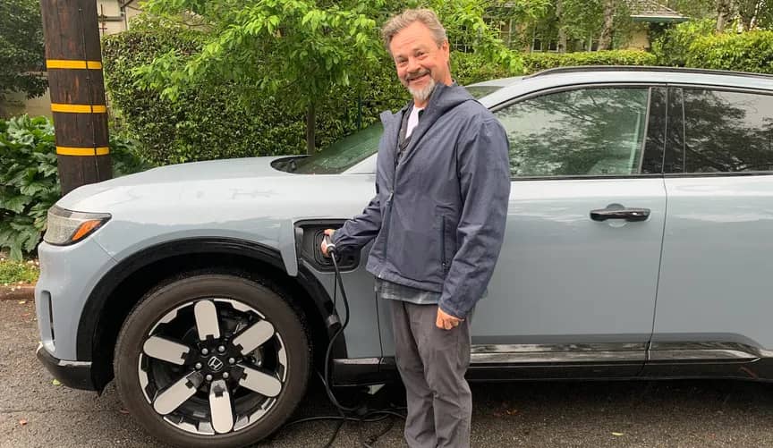 Person standing next to a grey car holding a charger